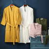 A yellow waffle knit robe and a white waffle knit robe hanging on a dark blue wall.