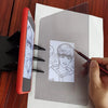 A hand draws on a transparent optical tracing board placed next to a red portable drawing projector.