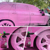 A pink car is being cleaned with a pressure washer foam cannon, showing dense white foam being applied to the wheel.