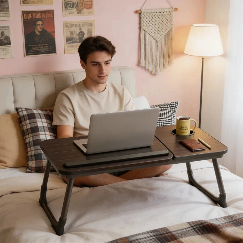 Un joven está sentado en una cama usando un escritorio portátil plegable para trabajar o estudiar.