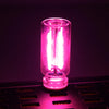 A glowing pink glass accent light bulb sitting on a black surface.