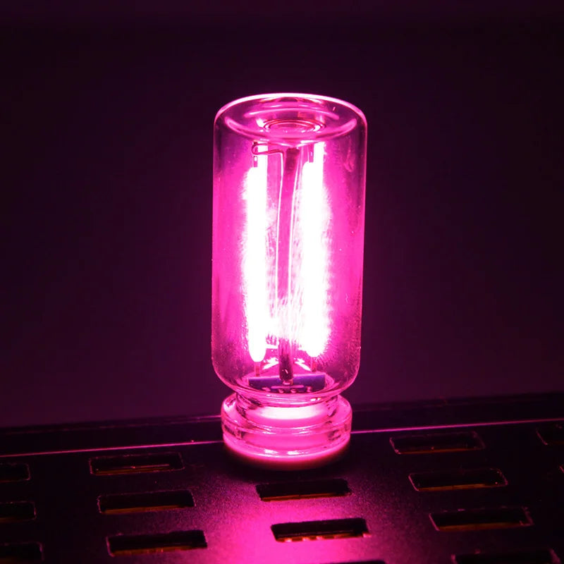 A glowing pink glass accent light bulb sitting on a black surface.