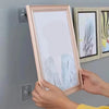 Hands are hanging a framed piece of art onto a wall using strong adhesive hooks.