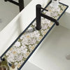 A black faucet mounted on a white countertop with a floral patterned mat featuring white and green roses.