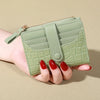 A hand holds a light green PU leather wallet with a zipper and card slots.
