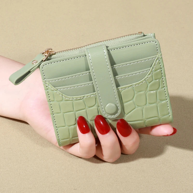 A hand holds a light green PU leather wallet with a zipper and card slots.