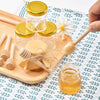 Hexagon mini glass honey jars with wood dippers and gold lids displayed on a wooden board.