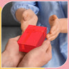 A pair of hands is holding a red velvet gift box with a bow, set against a blurred background.