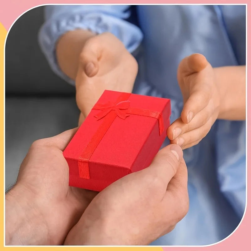 A pair of hands is holding a red velvet gift box with a bow, set against a blurred background.