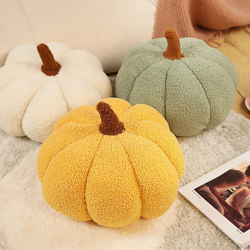 Three plush pumpkins in white, green, and yellow with brown stems resting on a fluffy surface.
