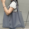 A person is holding a black and white striped foldable oxford cloth tote bag with a white sweater.