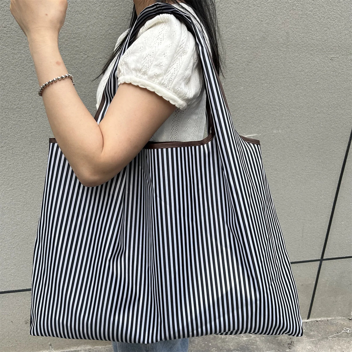 A person is holding a black and white striped foldable oxford cloth tote bag with a white sweater.