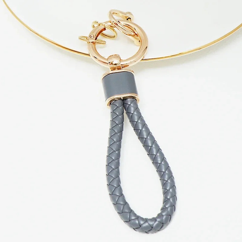 Gold chain necklace with a silver-toned pendant and a gray braided leather fob cover.