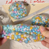 A hand holds a squishy sensory stress ball filled with multicolored soft plastic beads.