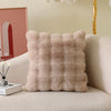 A fluffy beige decorative pillow cover with a textured, quilted pattern resting on a light-colored sofa.