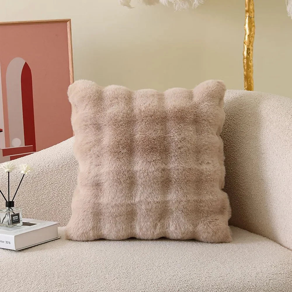 A fluffy beige decorative pillow cover with a textured, quilted pattern resting on a light-colored sofa.