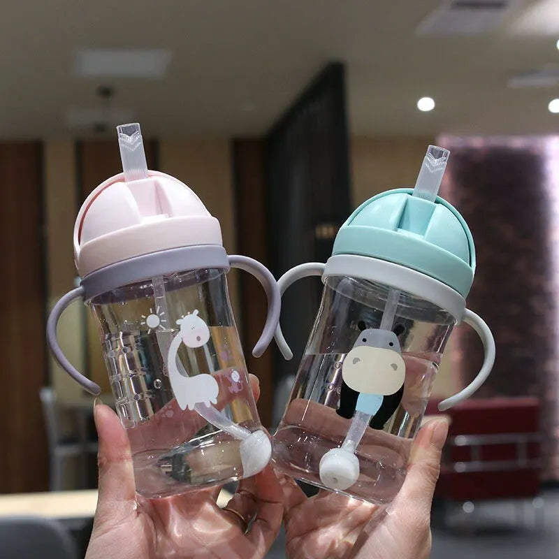 A hand holds a clear plastic sippy cup with a pink lid and a light blue straw, featuring a white animal design.