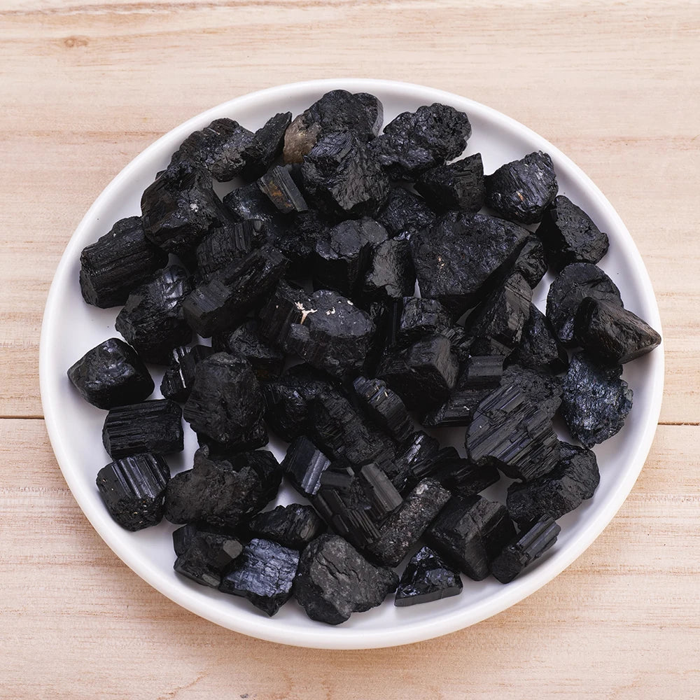 A pile of natural black tourmaline raw stone specimens on a white plate.