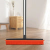 A rubber broom and carpet rake with an adjustable silver handle rests on a wooden floor.