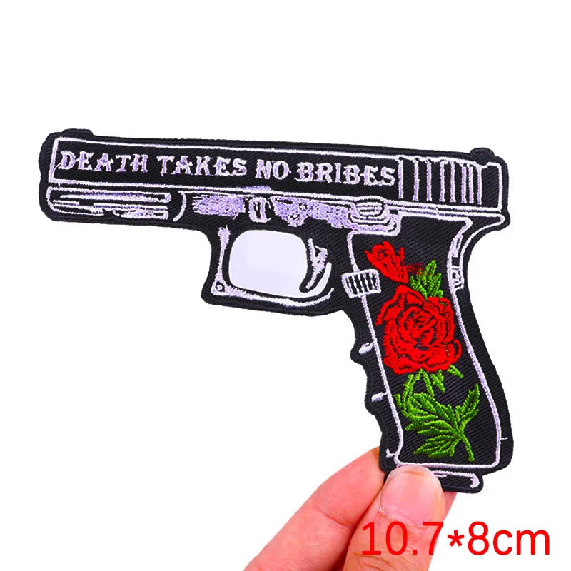 Black embroidered patch of a handgun with the text Death Takes No Ribes and a red rose design.