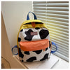 A yellow and black cow print backpack with an orange pocket resting on a white surface.