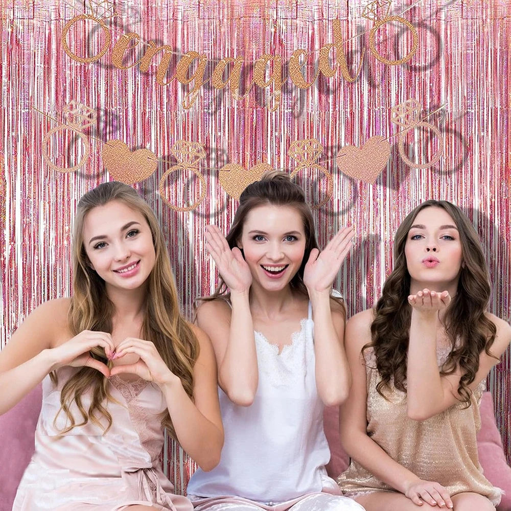 Tres mujeres jóvenes posando frente a un telón de fondo de cortina de flecos de papel metálico dorado rosa.