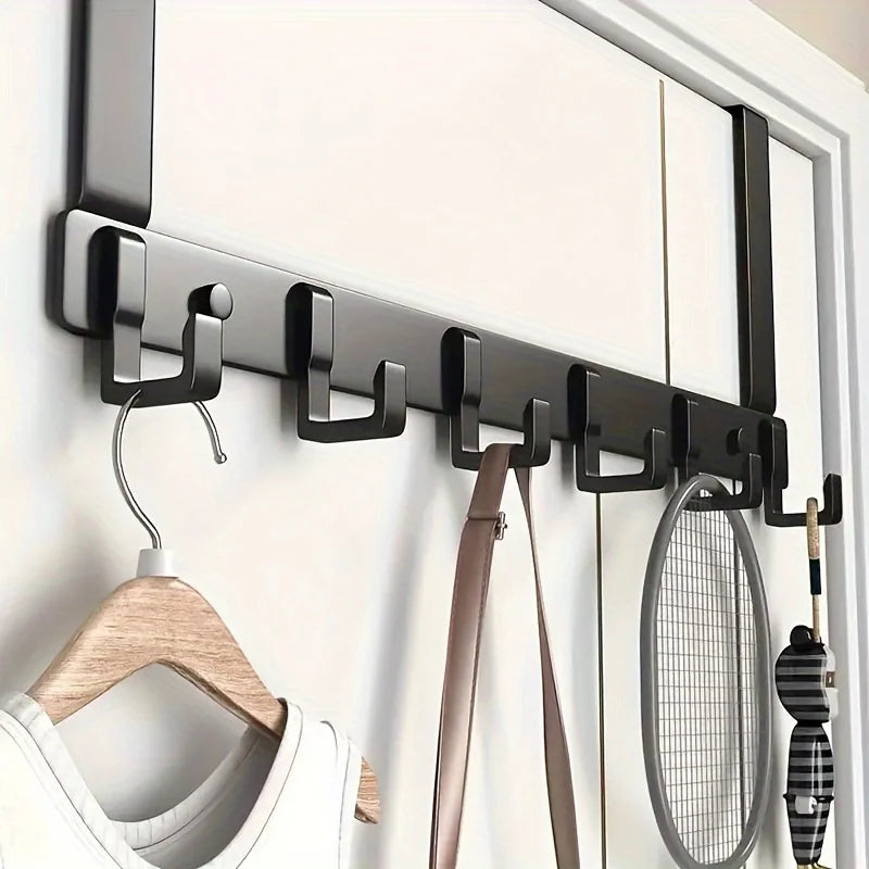 A black over-the-door coat rack with six hooks mounted on a white door, featuring a wooden hanger and a mesh sports bag.
