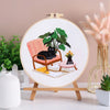 Embroidery kit featuring pre-printed floral and cat designs on a canvas mounted on a wooden easel.