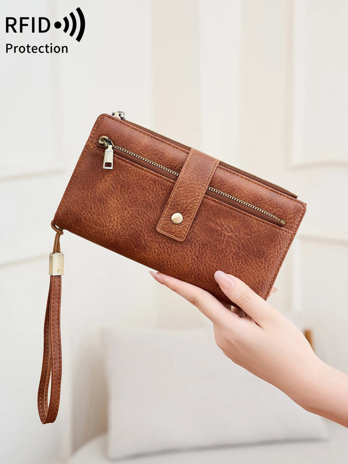 A brown PU leather long wallet with a zipper and leather strap is being held by a hand.