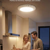A smart motion sensor light installed on a ceiling illuminates a kitchen area where a man and woman are preparing food.