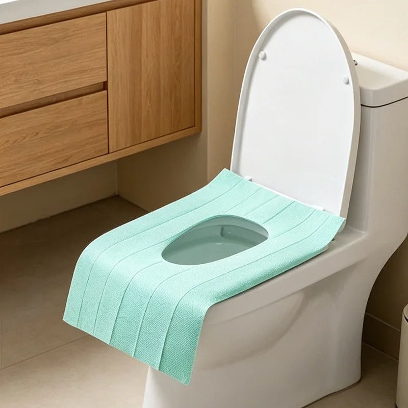 A white toilet features a light mint green disposable seat cover installed on the seat.