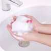Hands are lathering white foam on a white porcelain sink basin.