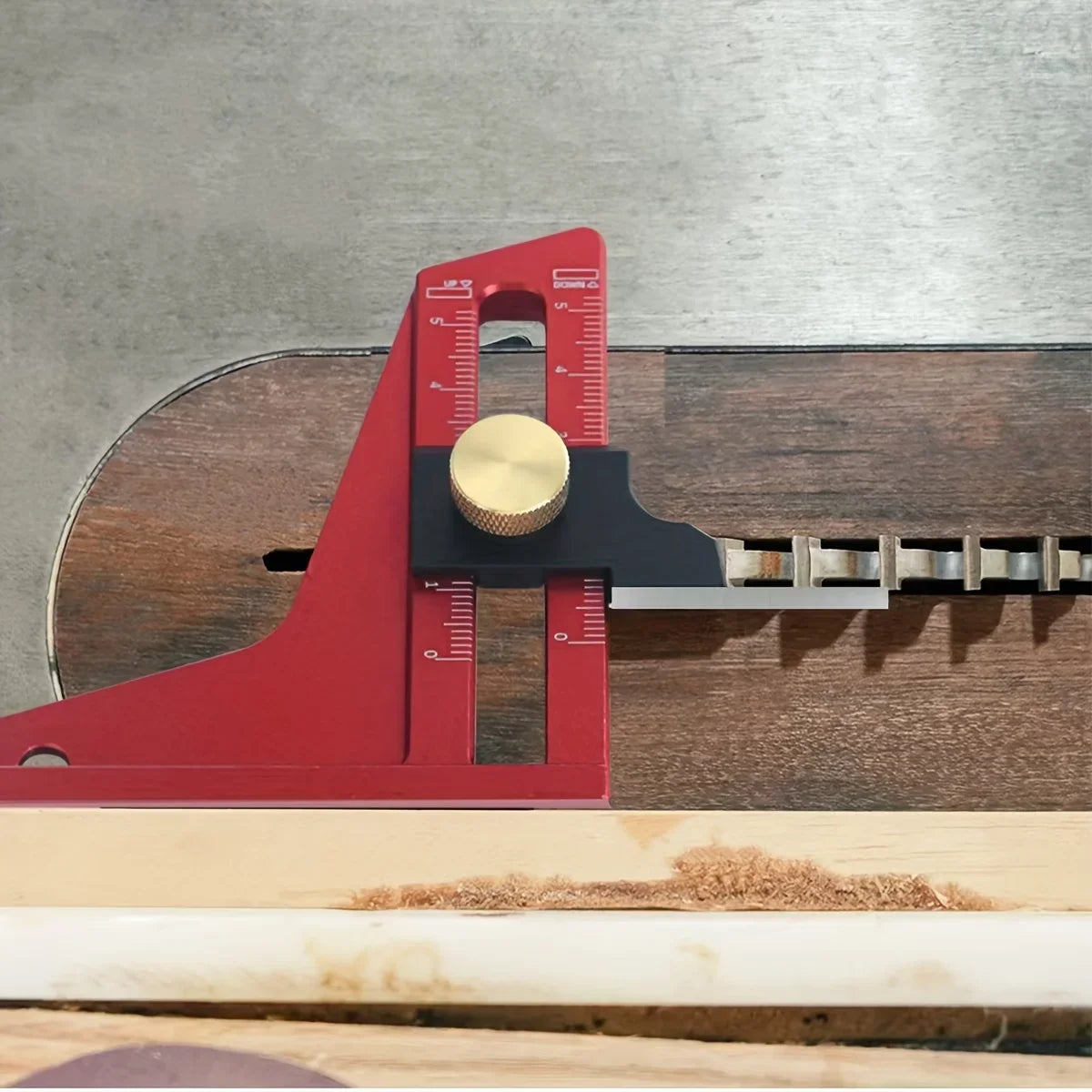 A red precision aluminum height setting gauge with a brass adjustment knob resting on a wooden table surface.