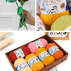 A collection of yellow and pink milk cotton blend yarn skeins displayed in a wooden box.