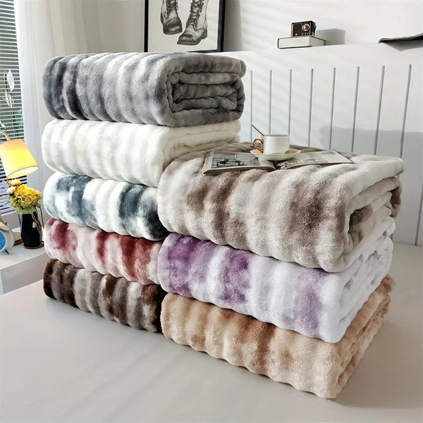 Ein Stapel von Plüsch-Faux-Pelz-Überwürfen in verschiedenen Graustufen, Beige- und Violetttönen auf einer weißen Oberfläche.
