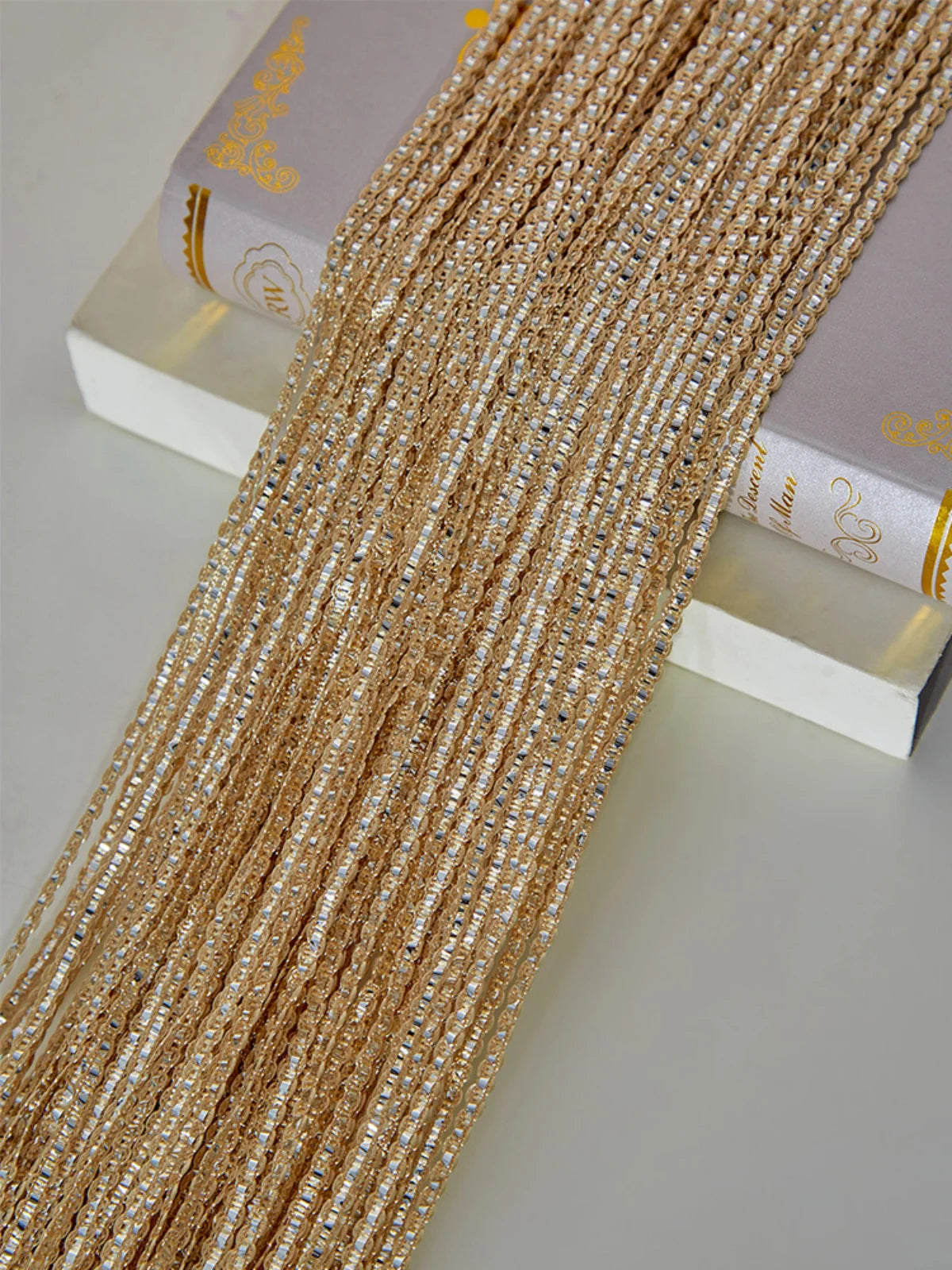 Gold-toned tassel string curtain made of small beads and threads displayed next to a book.