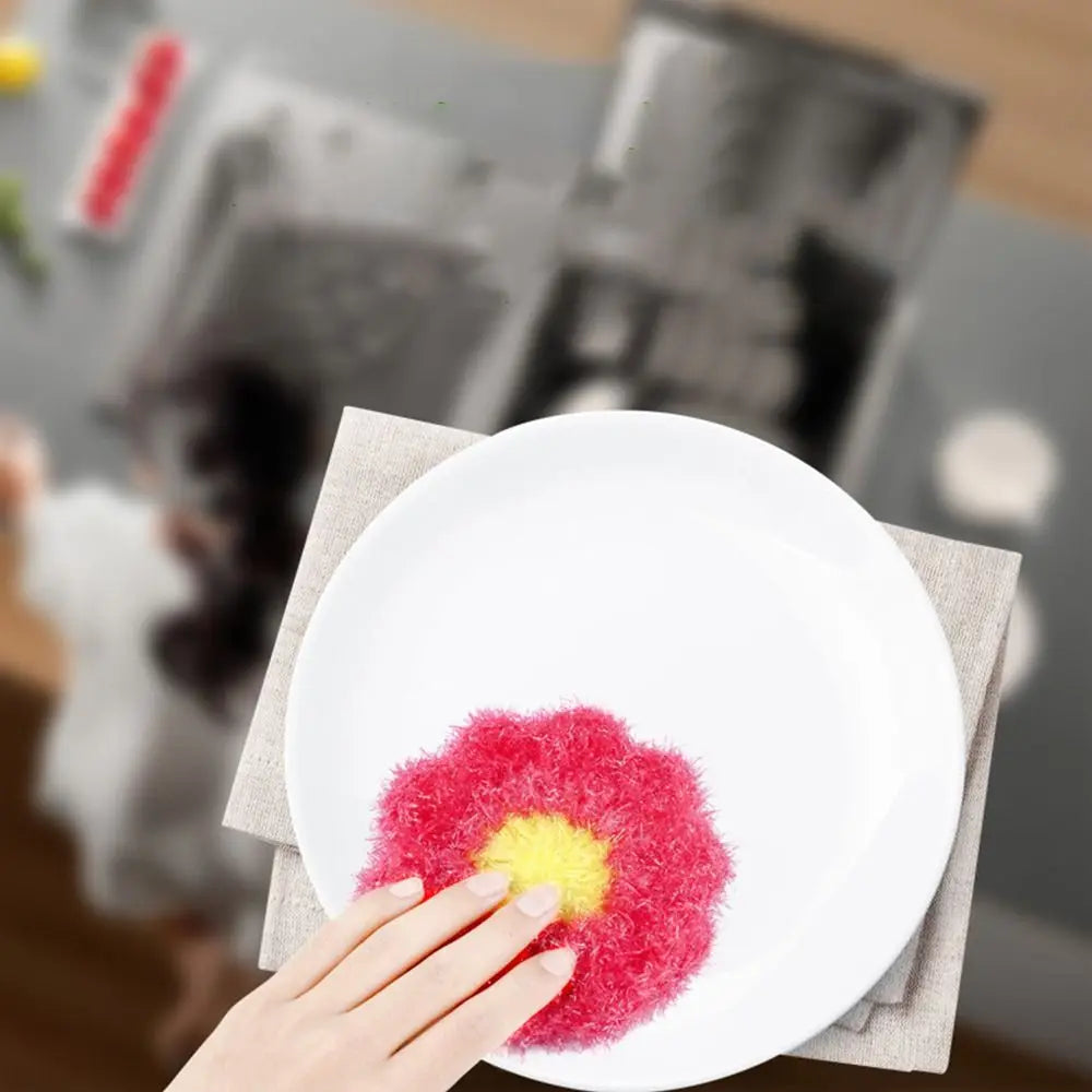 A hand places a bright red and yellow fluffy acrylic non-stick dish sponge on a white plate.