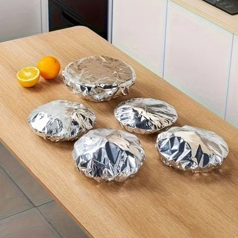 Mehrere wiederverwendbare Aluminium-Essverschlüsse auf einem Holztablett neben einer Orange.