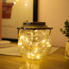 A glass solar lantern with a warm ambient glow sits on a wooden surface.