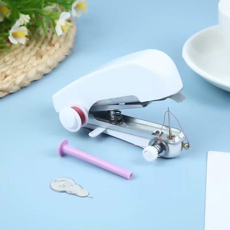 A white portable handheld sewing machine with a pink needle and thread visible on a light blue surface.