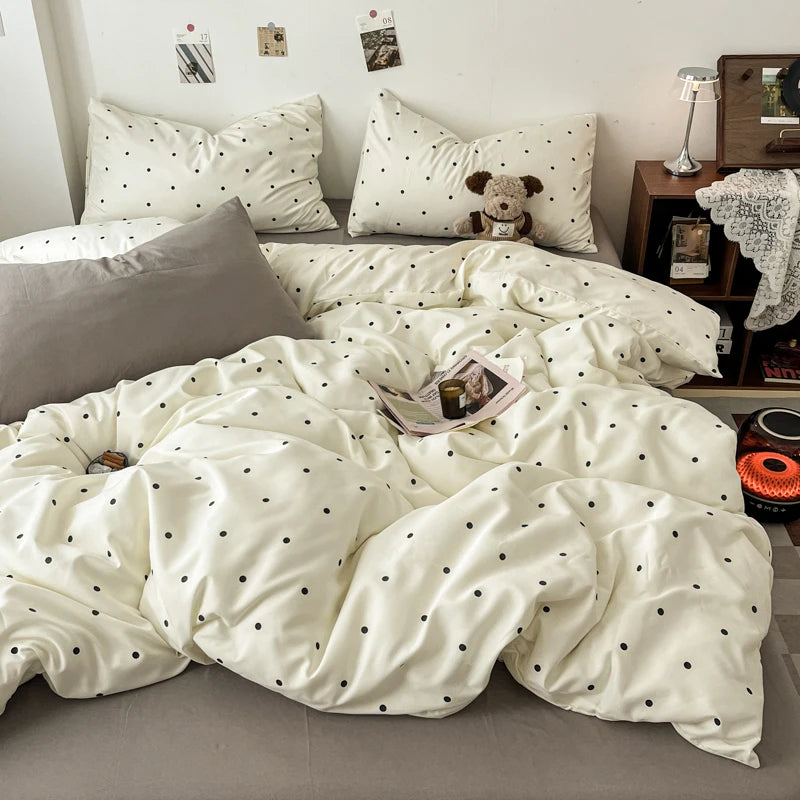 A white duvet cover set with black polka dots is displayed on a bed, alongside pillows and a stuffed animal.