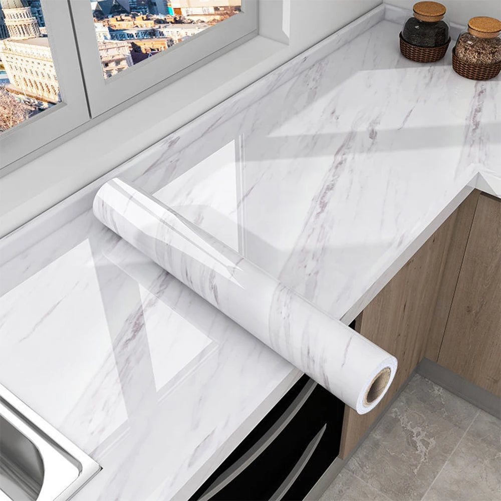 Roll of white marble peel-and-stick film displayed on a kitchen countertop with a window view.