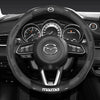 Close-up view of a black carbon fiber and leather steering wheel cover for a Mazda vehicle interior.