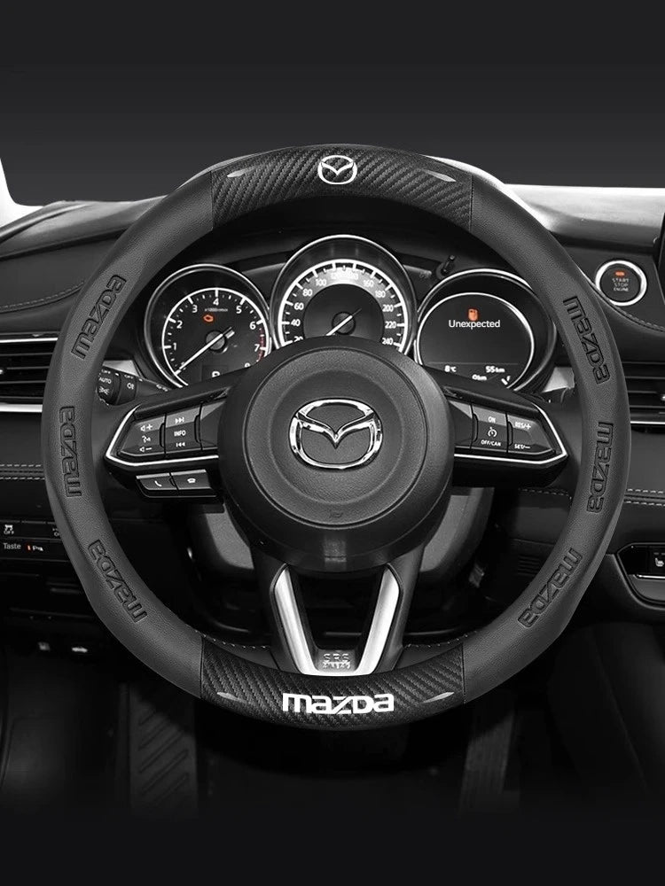 Close-up view of a black carbon fiber and leather steering wheel cover for a Mazda vehicle interior.