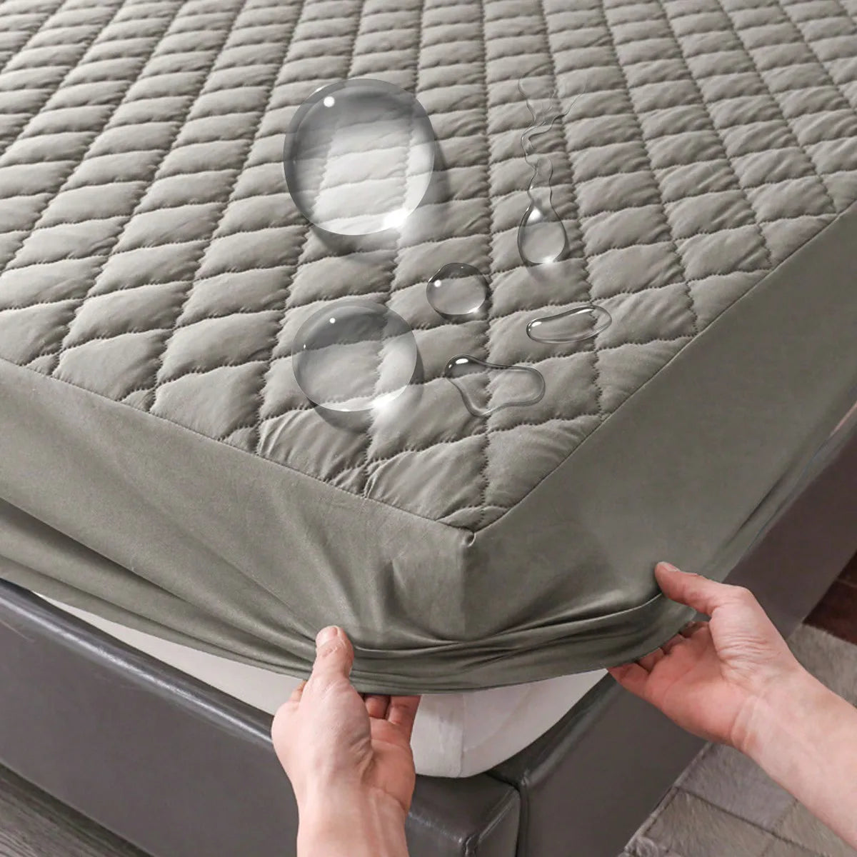 A close-up of a gray waterproof fitted mattress protector with visible water droplets on the surface.