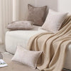 A beige chenille throw blanket draped over a white sofa with matching neutral-toned pillows.