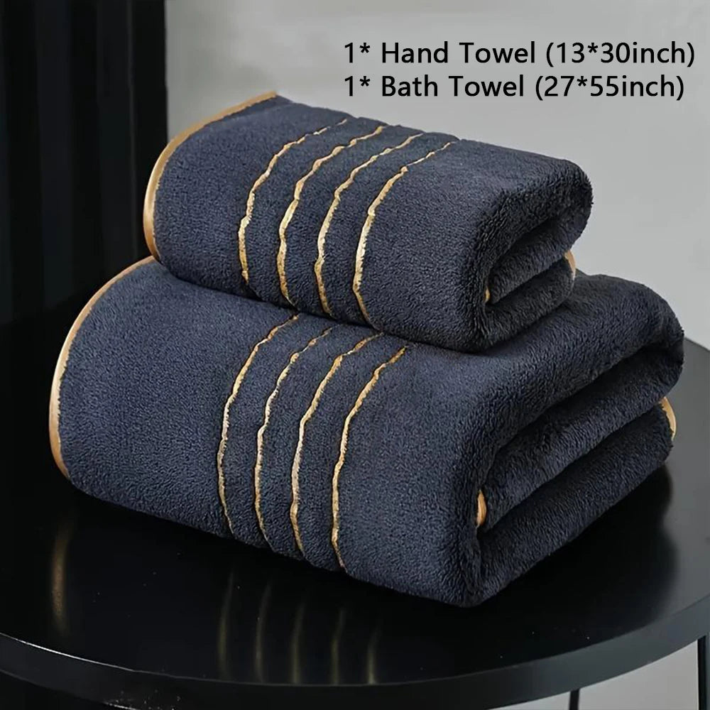 A stack of dark blue bath towels and hand towels with gold stripes displayed on a black surface.