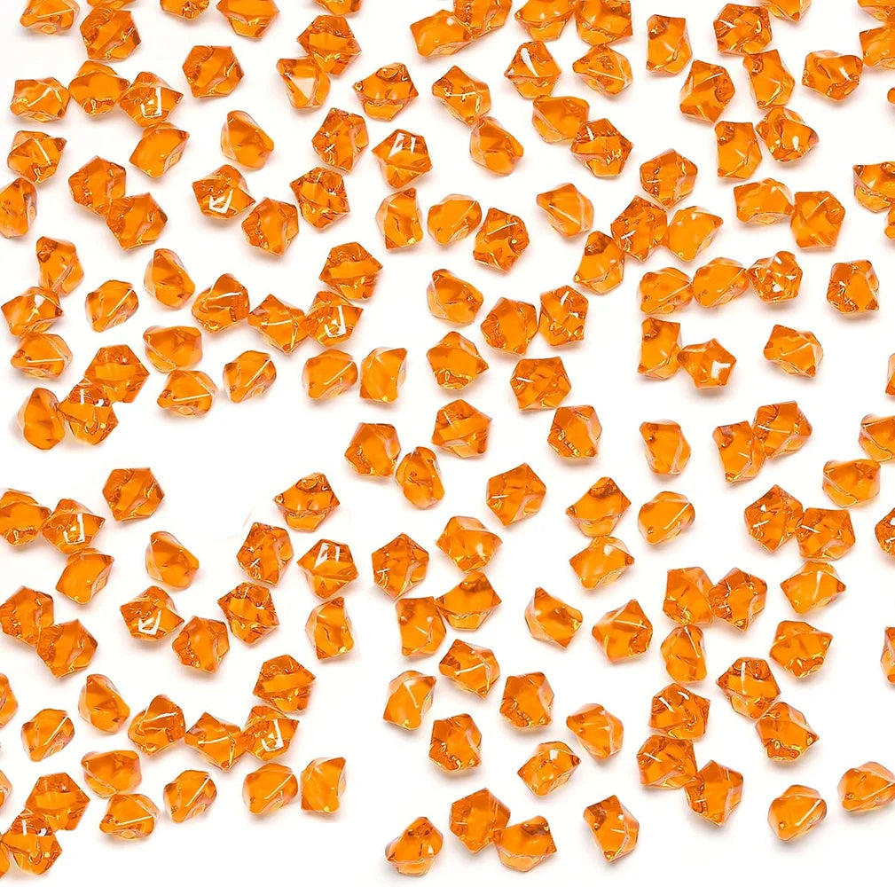 A pile of transparent orange acrylic crushed ice gems used for vase fillers and decor.
