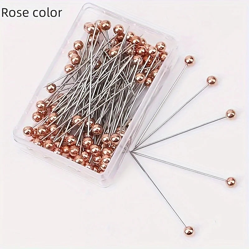 A clear plastic container filled with 100 rose gold precision quilting pins for sewing and crafting.