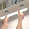 Hands are adjusting a white LED light bar with motion sensors mounted on a shelf.